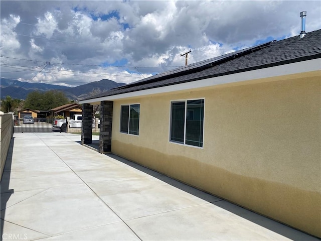 exterior space featuring fence, roof mounted solar panels, stucco siding, a mountain view, and a gate