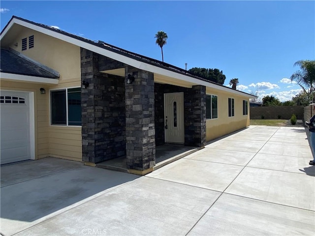 exterior space with fence, stone siding, and stucco siding