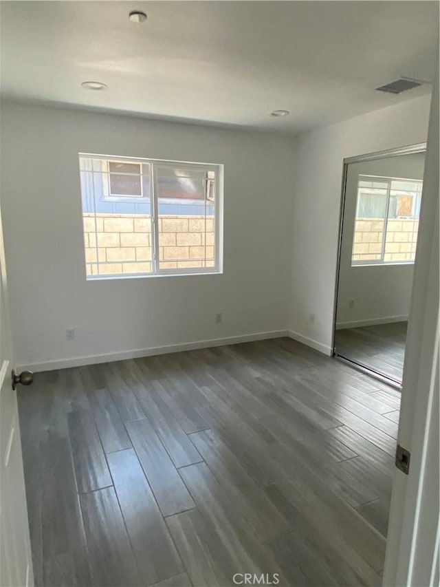 spare room with dark wood-style floors, visible vents, a healthy amount of sunlight, and baseboards