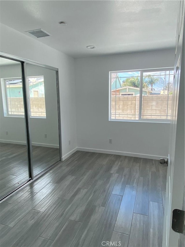 unfurnished bedroom featuring visible vents, baseboards, a closet, and wood finished floors