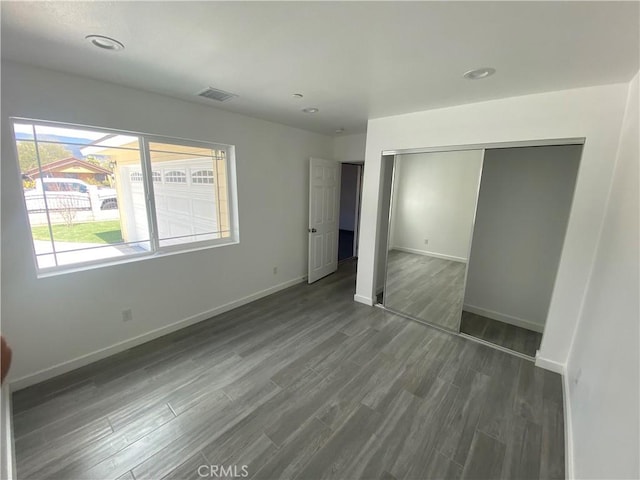 unfurnished bedroom with dark wood finished floors, visible vents, baseboards, and a closet