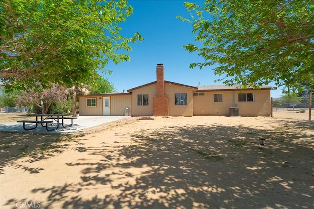 back of house with cooling unit, a chimney, fence, a patio area, and stucco siding