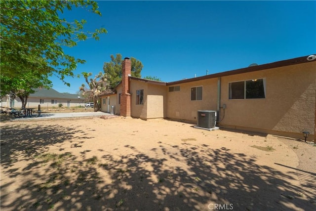 rear view of house with central AC, a chimney, stucco siding, and fence