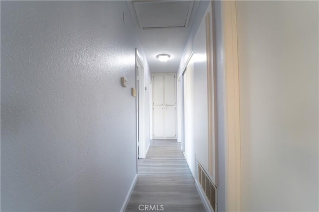 corridor featuring wood finished floors, visible vents, and baseboards
