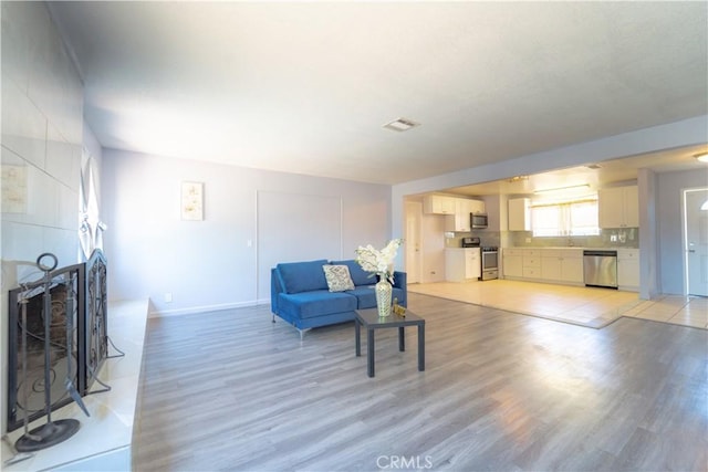 living area featuring light wood-type flooring, a tile fireplace, and baseboards