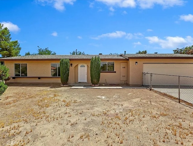 ranch-style house featuring an attached garage, concrete driveway, stucco siding, and fence