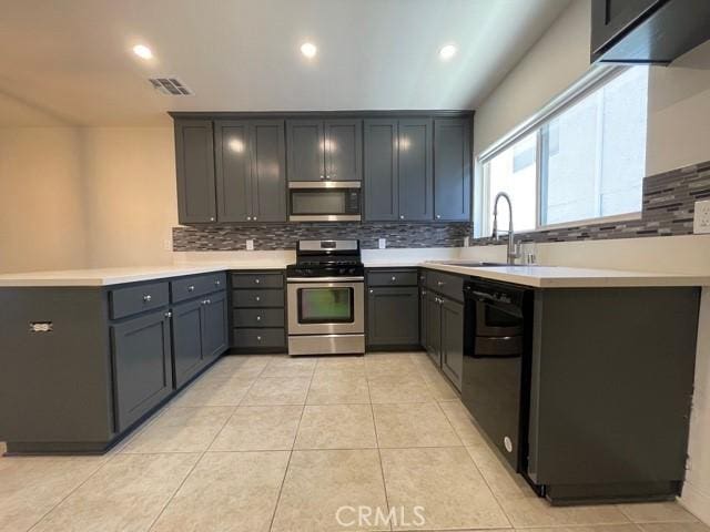 kitchen with a peninsula, a sink, decorative backsplash, light countertops, and appliances with stainless steel finishes