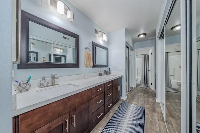 bathroom with visible vents, double vanity, wood finished floors, toilet, and a sink
