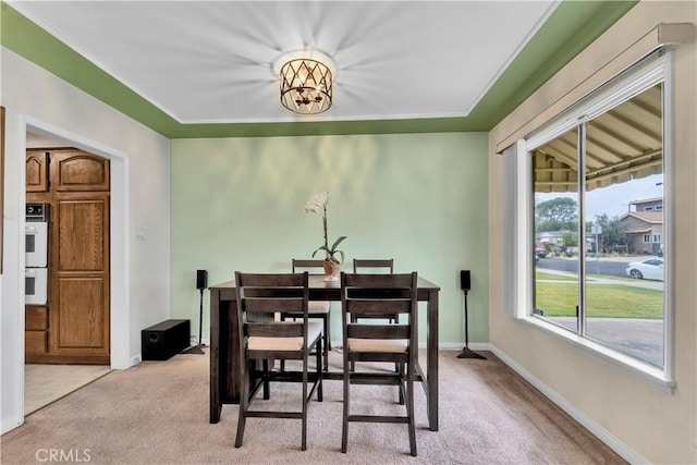 dining area with a notable chandelier, light colored carpet, and baseboards