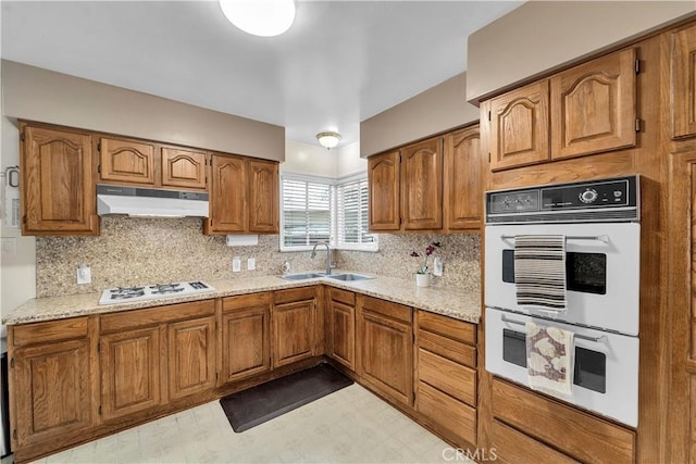 kitchen featuring brown cabinets, under cabinet range hood, a sink, white appliances, and light floors