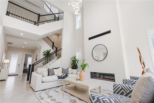 living area featuring stairway, visible vents, a high ceiling, recessed lighting, and a glass covered fireplace