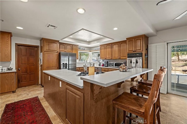 kitchen featuring visible vents, stainless steel appliances, brown cabinetry, light countertops, and a raised ceiling