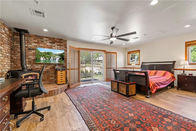 bedroom featuring visible vents, multiple windows, a wood stove, and wood finished floors