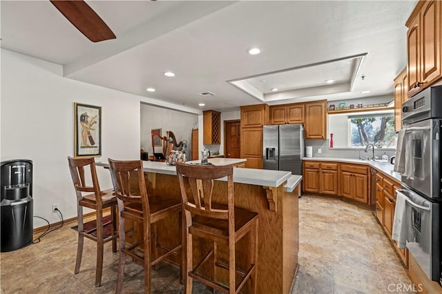 kitchen featuring a breakfast bar area, brown cabinetry, light countertops, appliances with stainless steel finishes, and a raised ceiling