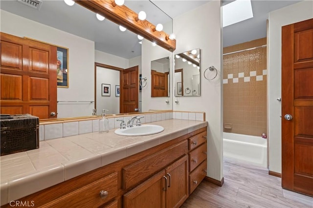 full bathroom featuring vanity, wood finished floors, baseboards, visible vents, and tub / shower combination