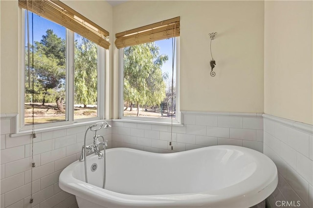 bathroom with a wainscoted wall, a soaking tub, and tile walls