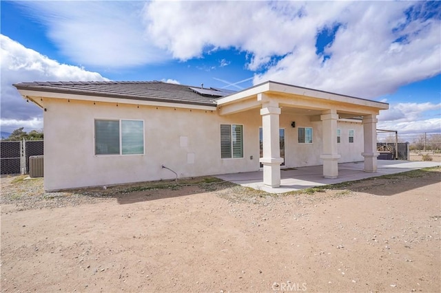 rear view of property featuring fence, a tile roof, roof mounted solar panels, stucco siding, and a patio area