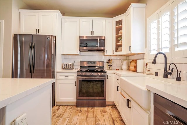 kitchen featuring tasteful backsplash, light wood finished floors, appliances with stainless steel finishes, white cabinets, and a sink