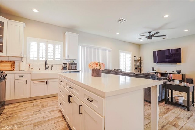 kitchen featuring wood finish floors, ceiling fan, a sink, open floor plan, and backsplash