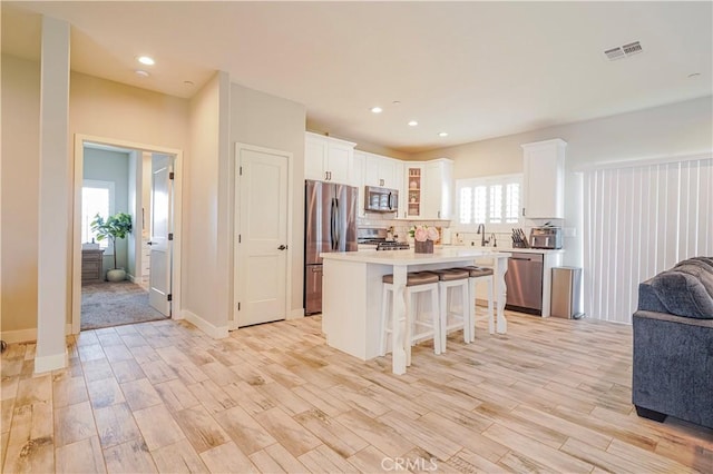 kitchen with open floor plan, white cabinetry, stainless steel appliances, a breakfast bar area, and light countertops