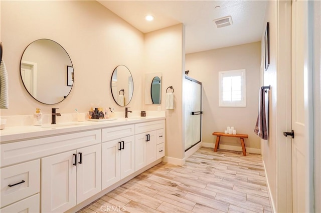 full bathroom with double vanity, a shower stall, wood finished floors, and a sink