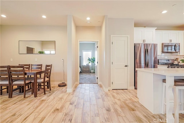 kitchen featuring stainless steel appliances, light wood-style flooring, decorative backsplash, and light countertops