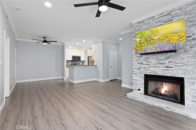 unfurnished living room with a stone fireplace, crown molding, wood finished floors, and a ceiling fan