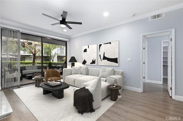 living area with wood finished floors, baseboards, a ceiling fan, visible vents, and ornamental molding