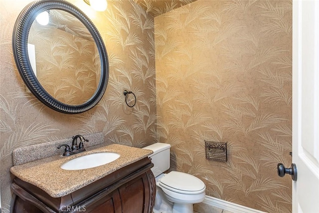 bathroom with toilet, vanity, and wallpapered walls