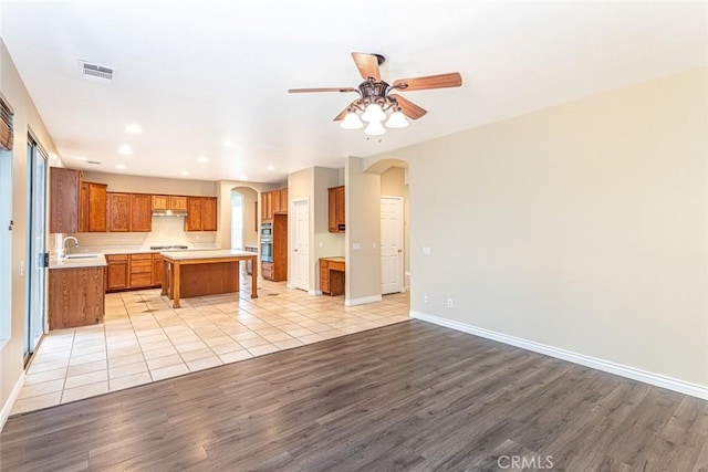 kitchen with visible vents, brown cabinets, a ceiling fan, open floor plan, and arched walkways