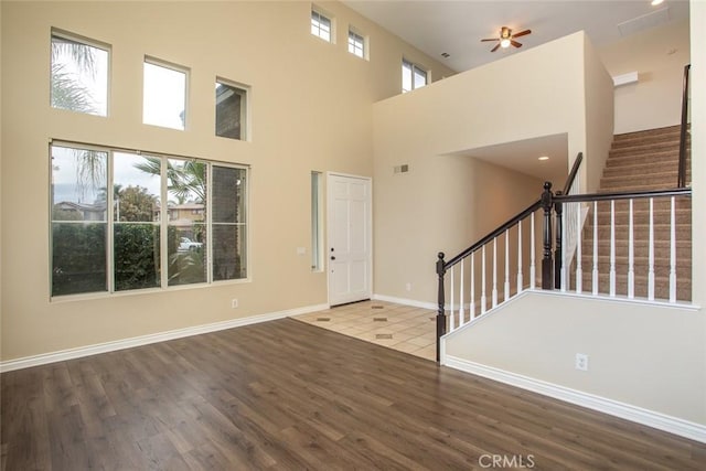 foyer entrance featuring baseboards, stairs, a high ceiling, wood finished floors, and a ceiling fan