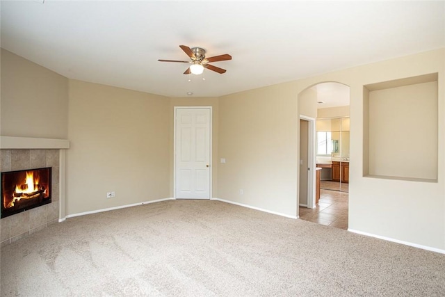 unfurnished living room featuring a ceiling fan, arched walkways, carpet, baseboards, and a tile fireplace