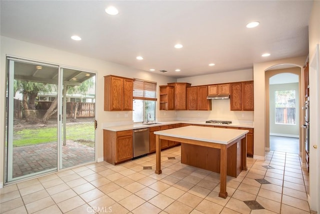 kitchen with a kitchen island, brown cabinetry, light countertops, arched walkways, and stainless steel appliances