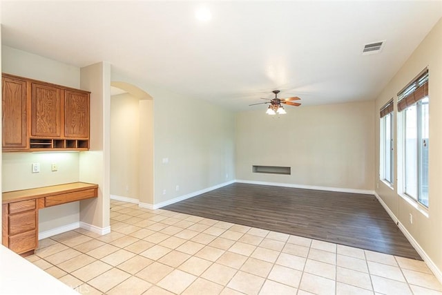 unfurnished living room with visible vents, arched walkways, baseboards, and a ceiling fan