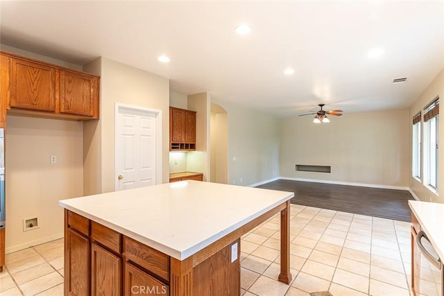 kitchen with visible vents, a kitchen island, arched walkways, ceiling fan, and brown cabinets