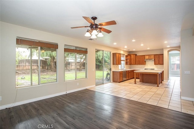 kitchen featuring ceiling fan, light countertops, brown cabinets, arched walkways, and stainless steel dishwasher