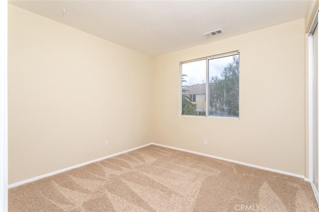 empty room with baseboards, visible vents, and light carpet