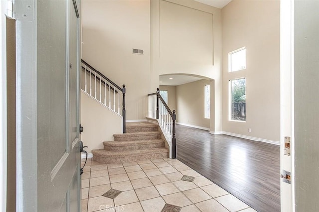 foyer entrance featuring visible vents, light wood finished floors, baseboards, a high ceiling, and arched walkways