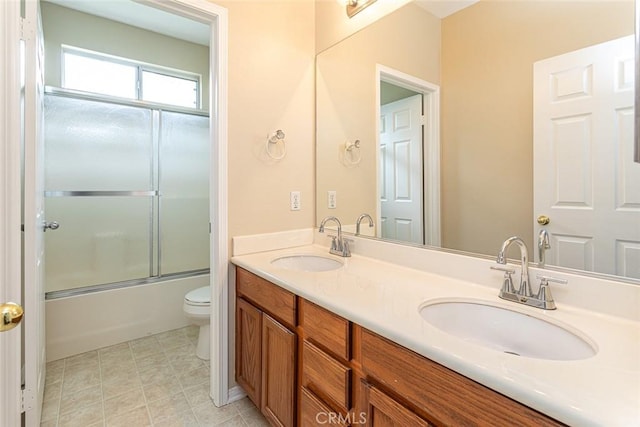 bathroom featuring double vanity, toilet, bath / shower combo with glass door, and a sink