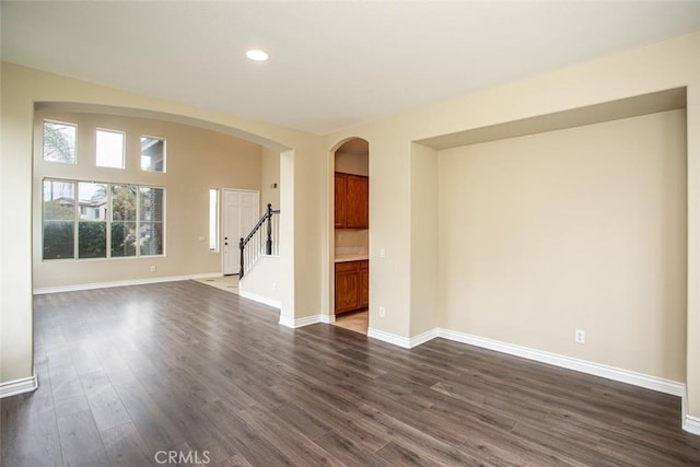 spare room featuring stairway, dark wood-style floors, arched walkways, and baseboards