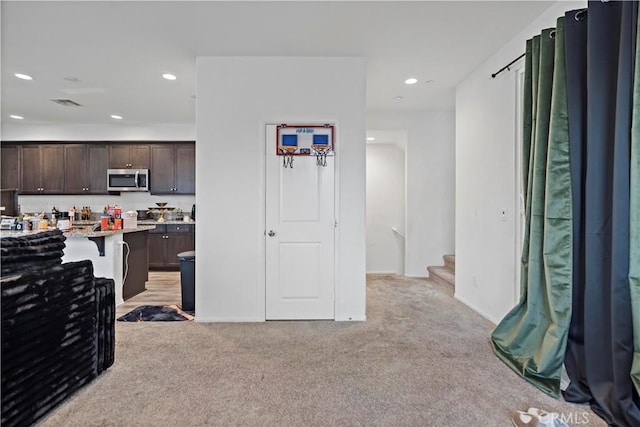 kitchen featuring recessed lighting, stainless steel microwave, dark brown cabinetry, and light colored carpet