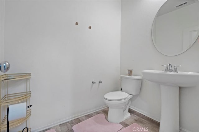 half bathroom with visible vents, baseboards, toilet, wood finished floors, and a sink