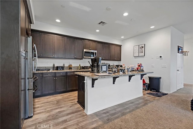 kitchen featuring visible vents, a breakfast bar, light stone counters, stainless steel appliances, and dark brown cabinetry