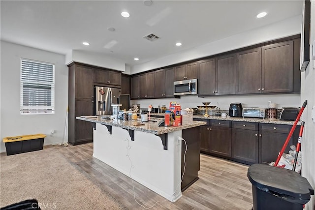 kitchen featuring visible vents, a kitchen bar, light stone counters, dark brown cabinetry, and appliances with stainless steel finishes