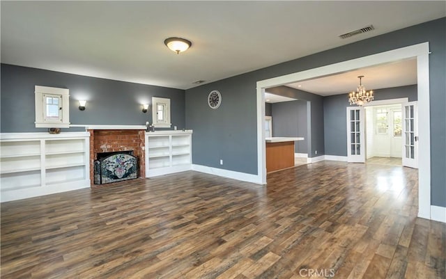 unfurnished living room featuring wood finished floors, baseboards, visible vents, a brick fireplace, and a chandelier