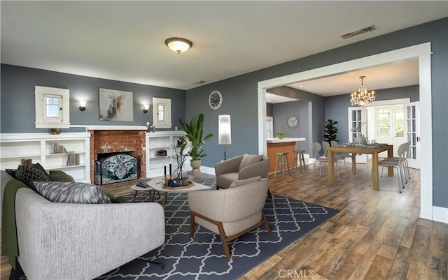 living room with visible vents, a brick fireplace, baseboards, wood finished floors, and a notable chandelier