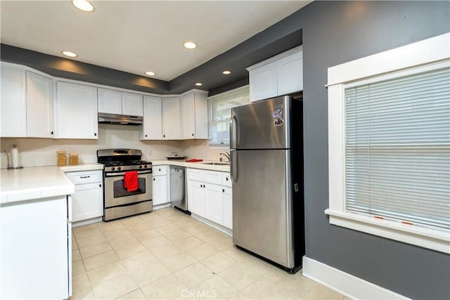 kitchen featuring under cabinet range hood, white cabinetry, recessed lighting, stainless steel appliances, and tile counters