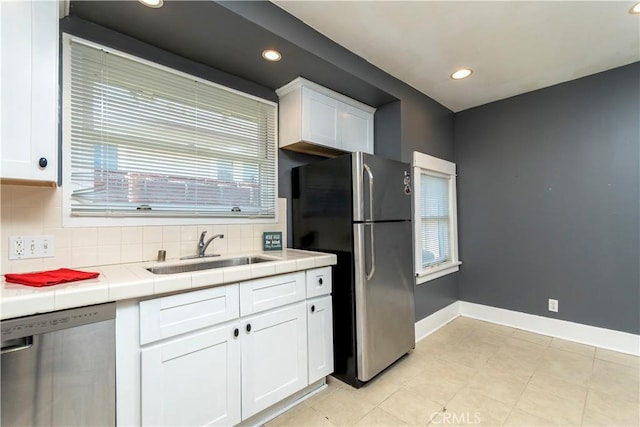 kitchen featuring a sink, appliances with stainless steel finishes, tile counters, and white cabinetry