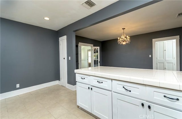 kitchen featuring visible vents, a notable chandelier, white cabinetry, tile countertops, and baseboards