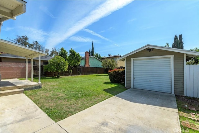 view of yard featuring an outbuilding, concrete driveway, fence, and a garage